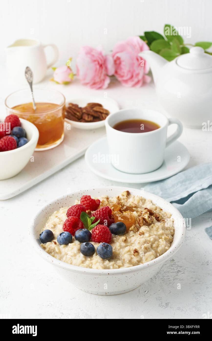 Bouillie d'avoine avec myrtille, framboises, confiture et noix dans un bol blanc, régime de tirets avec des baies, fond blanc, vue de côté, verticale. Alimentation saine Banque D'Images