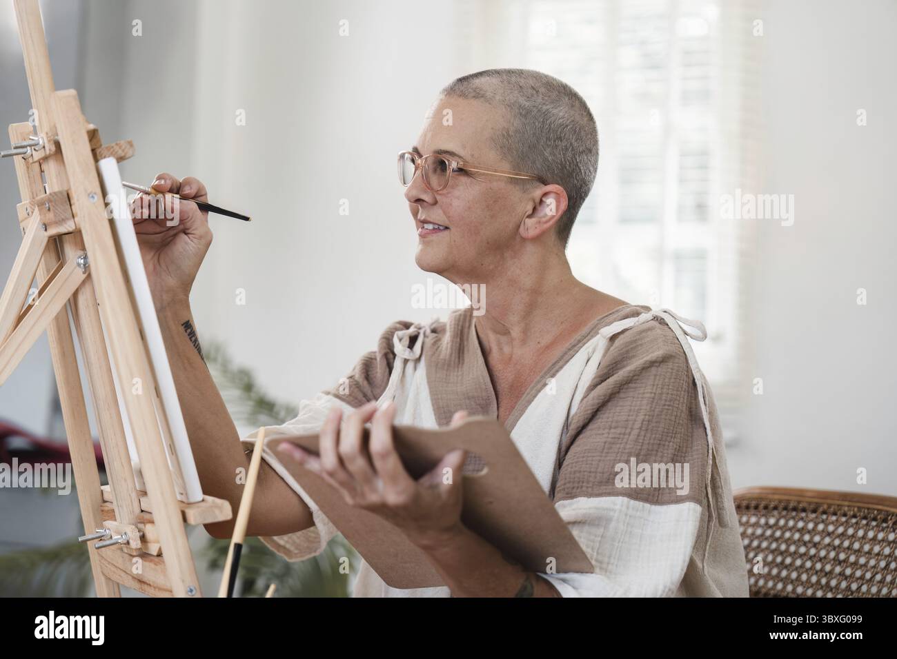 Femme âgée artiste peignant sur toile dans un studio bien éclairé, mettant en valeur la créativité et la passion pour l'art. Banque D'Images
