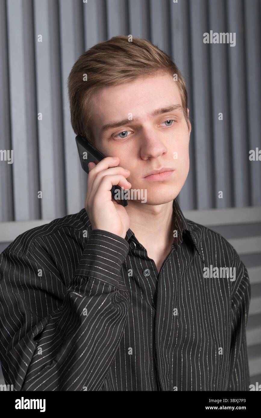 Triste jeune homme dans une chemise noire parlant au téléphone portable sur un fond sombre Banque D'Images