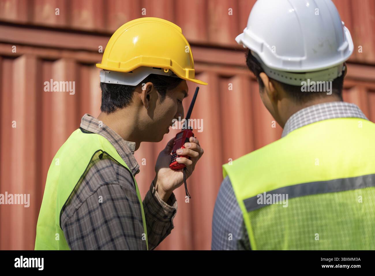 Deux ingénieurs en construction travaillant sur les équipements de sécurité examinent les plans tout en discutant de la logistique à l'aide d'un talkie-walkie Banque D'Images