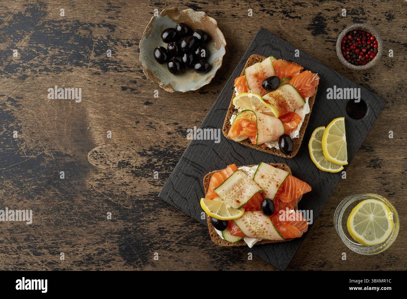 Smorrebrod - sandwichs traditionnels danois.Pain de seigle noir avec saumon, fromage à la crème, concombre et olives sur fond de bois brun foncé Banque D'Images