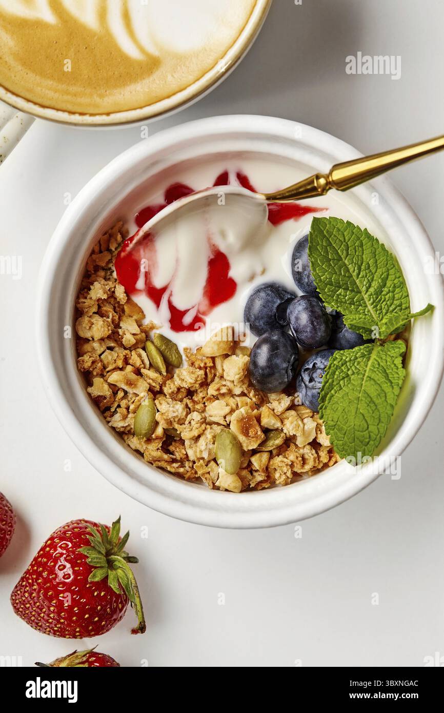 Profitez d'un petit déjeuner nutritif avec yaourt, granola, baies fraîches, et une tasse de café avec latte art. Banque D'Images