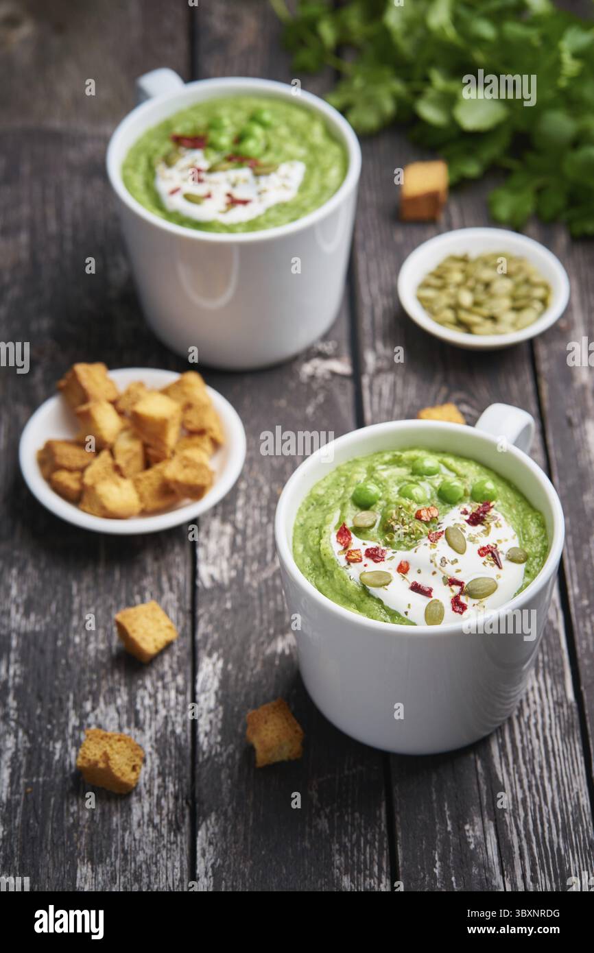 Soupe à la crème de brocoli, verticale. Purée de légumes verts dans deux grandes tasses blanches. Alimentation de la soupe végétalienne de brocoli, courgettes, pois verts sur fond de bois foncé Banque D'Images