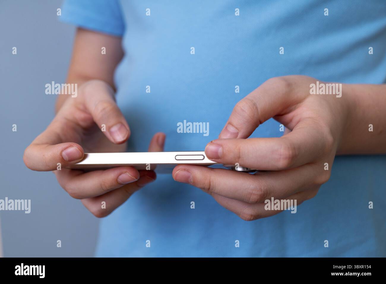 Jeune femme caucasienne texturant sur smartphone dans une chemise bleue décontractée Banque D'Images