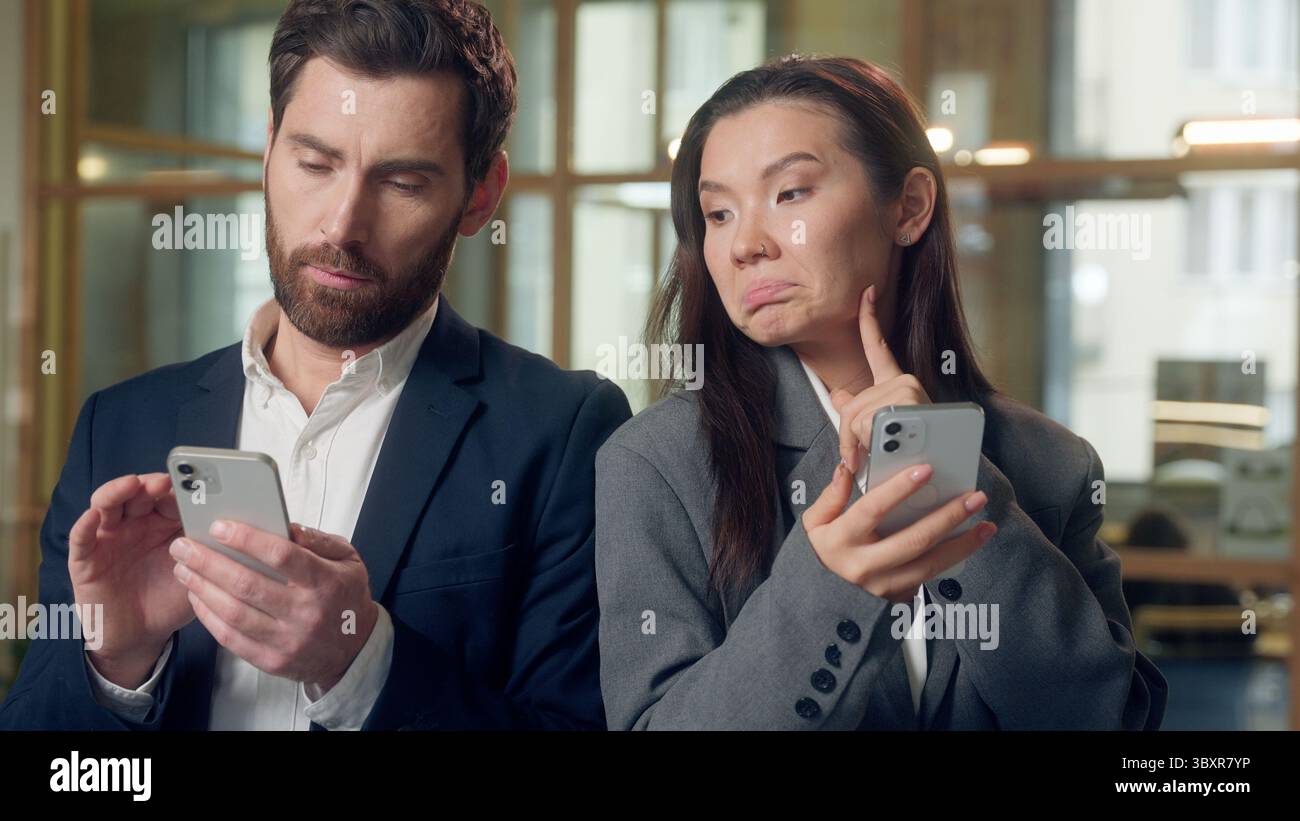 Collègues d'affaires de bureau multiethnique cherchant en ligne smartphone Internet coréen femme réfléchie défilement téléphone mobile secouant le doigt pas caucasien Banque D'Images