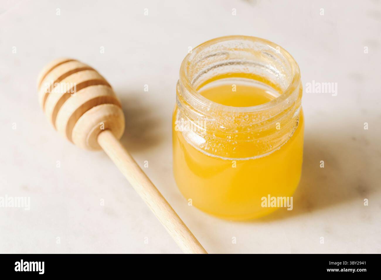 Miel frais dans un bocal en verre. Douceur naturelle avec un plongeur de miel sur fond de marbre. Produit biologique sain riche en nutriments. Texture liquide dorée Banque D'Images