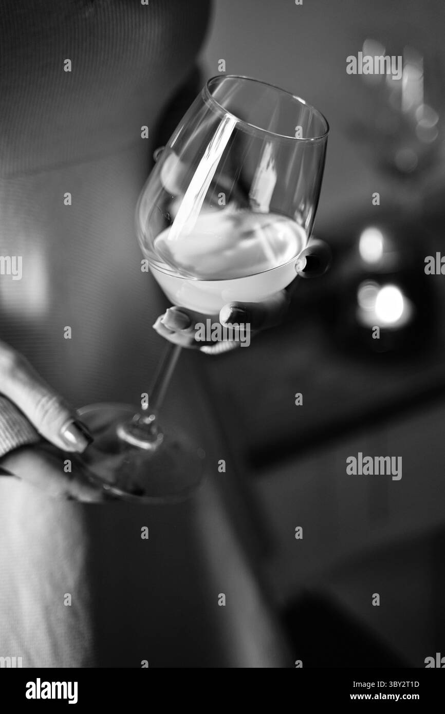 Une femme tient gracieusement un verre de vin blanc, capturant magnifiquement le reflet des chandelles dans un cadre monochrome, exsudant l'élégance et la sophistication Banque D'Images