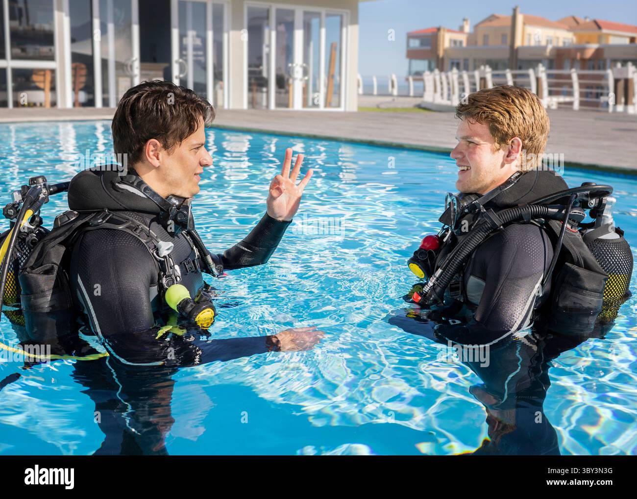 Deux plongeurs dans une piscine dans un complexe de plongée en combinaisons et équipement de plongée. Formateur montrant le signal OK à un élève souriant Banque D'Images