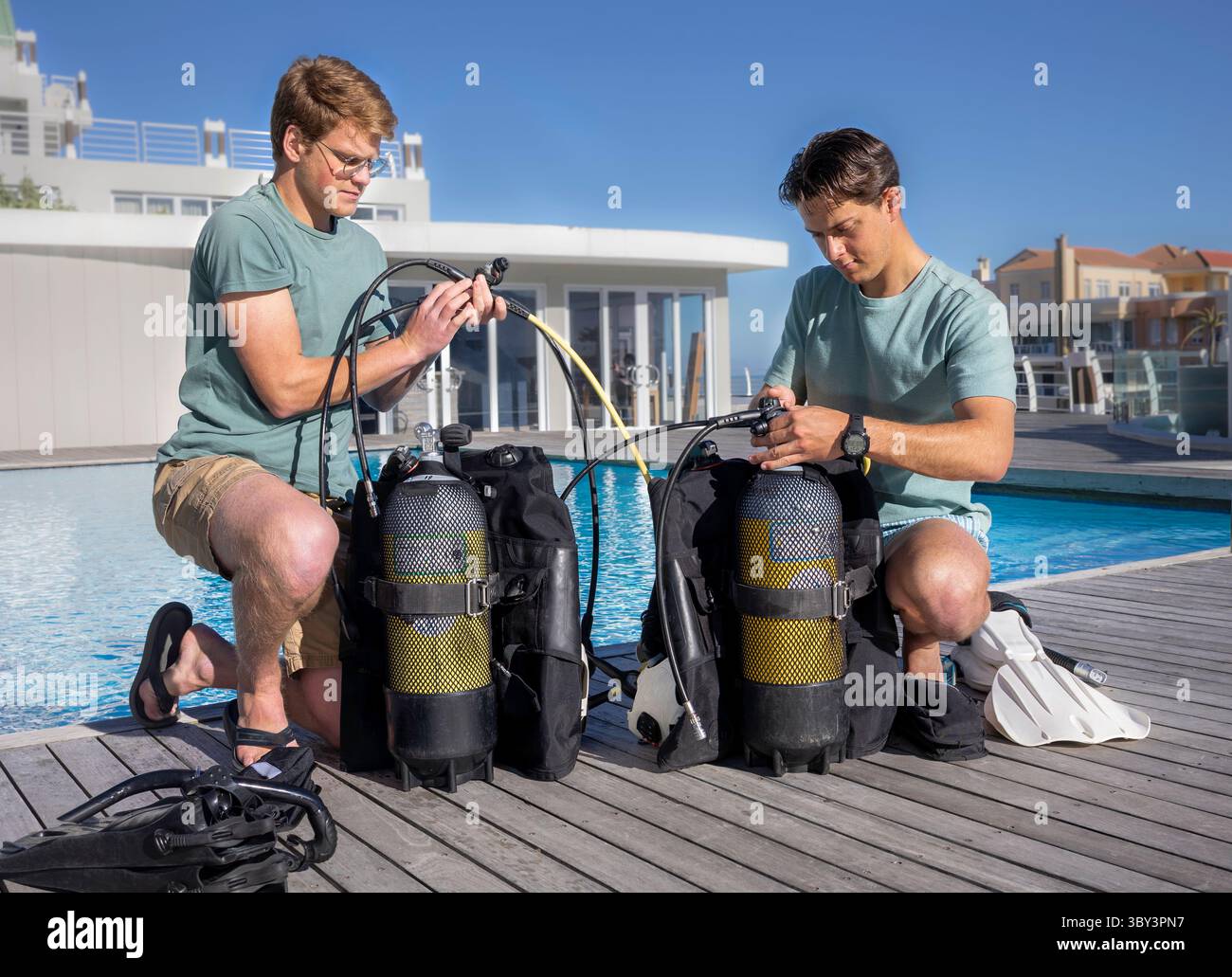 Deux plongeurs portant des vêtements d'été préparent leur équipement près d'une piscine dans un centre de plongée. Fixation de leurs régulateurs aux vérins. Banque D'Images