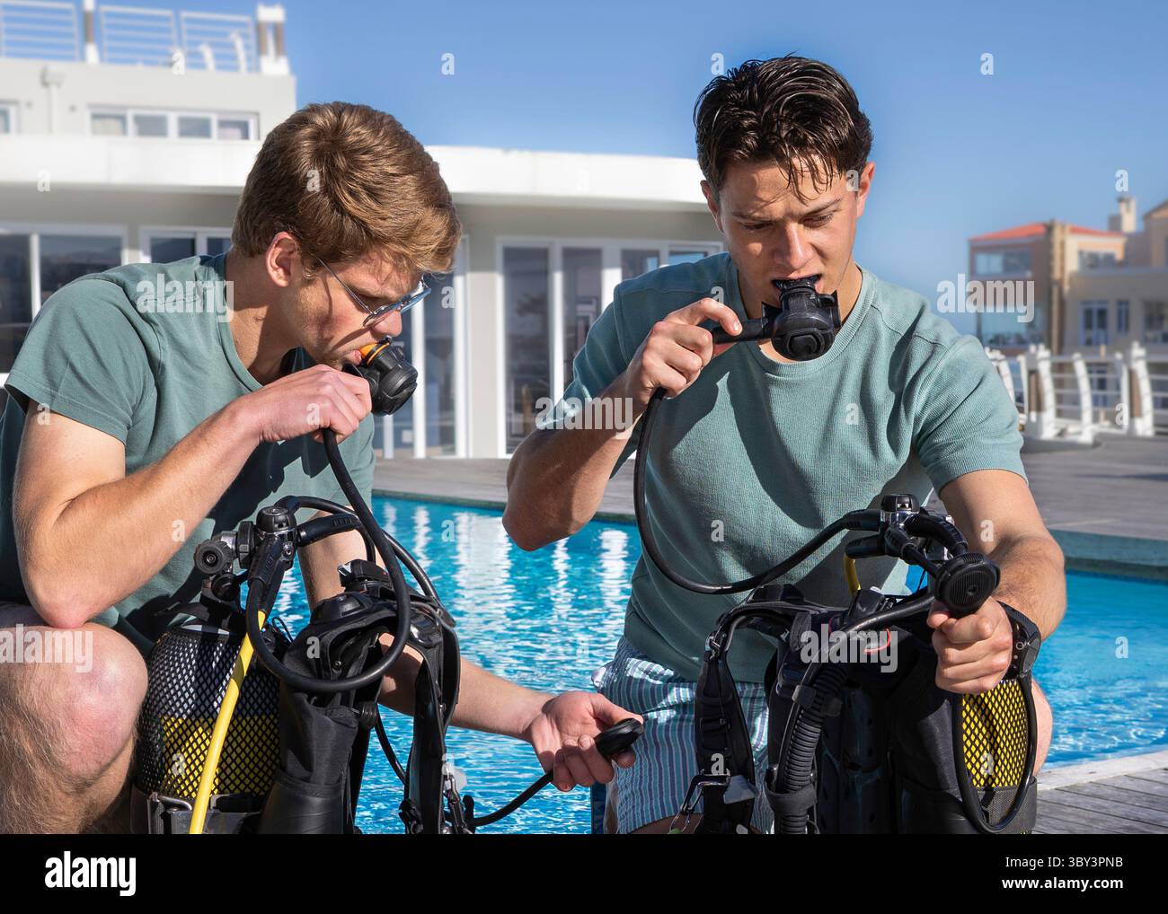 Gros plan de deux plongeurs portant des vêtements d'été préparent leur équipement près d'une piscine dans un centre de plongée. Tester leurs régulateurs et checkin Banque D'Images