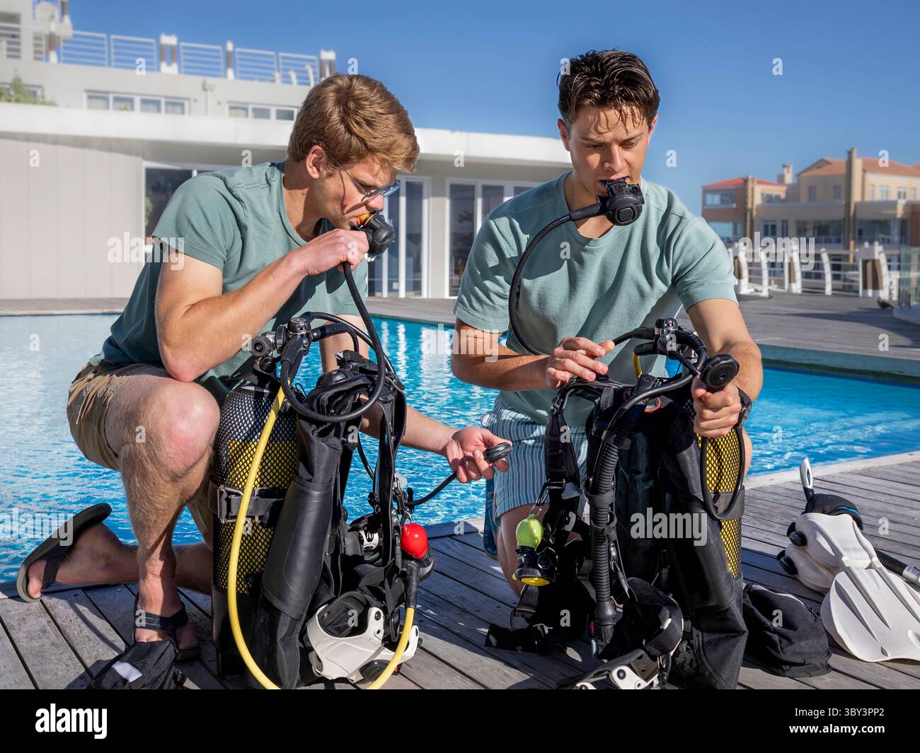 Deux plongeurs portant des vêtements d'été préparent leur équipement près d'une piscine dans un centre de plongée. Tester leurs régulateurs et contrôler leur air Banque D'Images