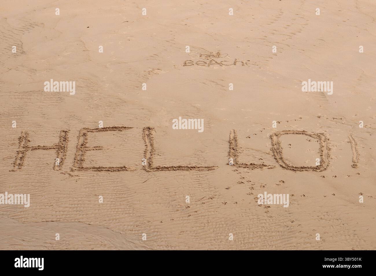 Un « Bonjour ! » Salutation écrite en majuscules sur une plage de sable à marée basse avec un plus petit 'Hello Beach !' salutation écrite ci-dessus Banque D'Images