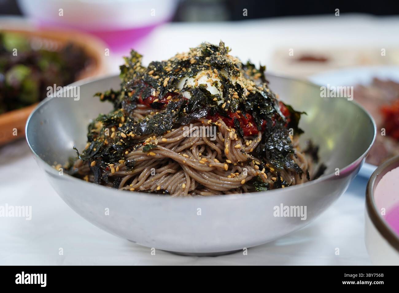 Gros plan de nouilles de sarrasin coréennes avec sauce épicée et légumes dans un bol en métal Banque D'Images