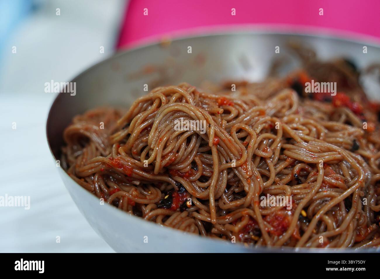 Gros plan de nouilles de sarrasin coréennes avec sauce épicée et légumes dans un bol en métal Banque D'Images