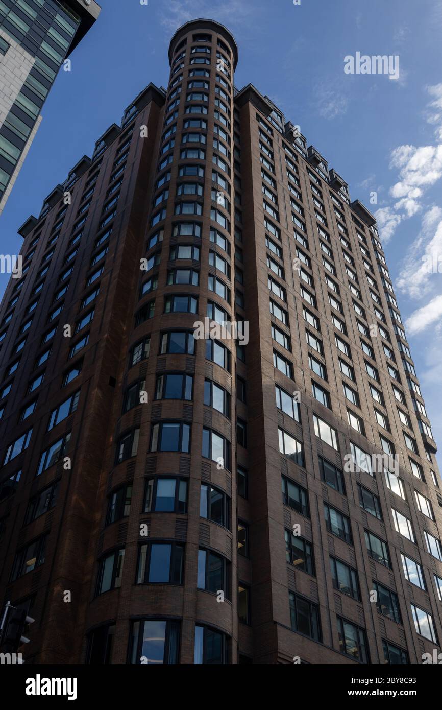 Gratte-ciel moderne en briques cylindriques, orné de grandes fenêtres en verre, placé sur un ciel bleu clair. Banque D'Images