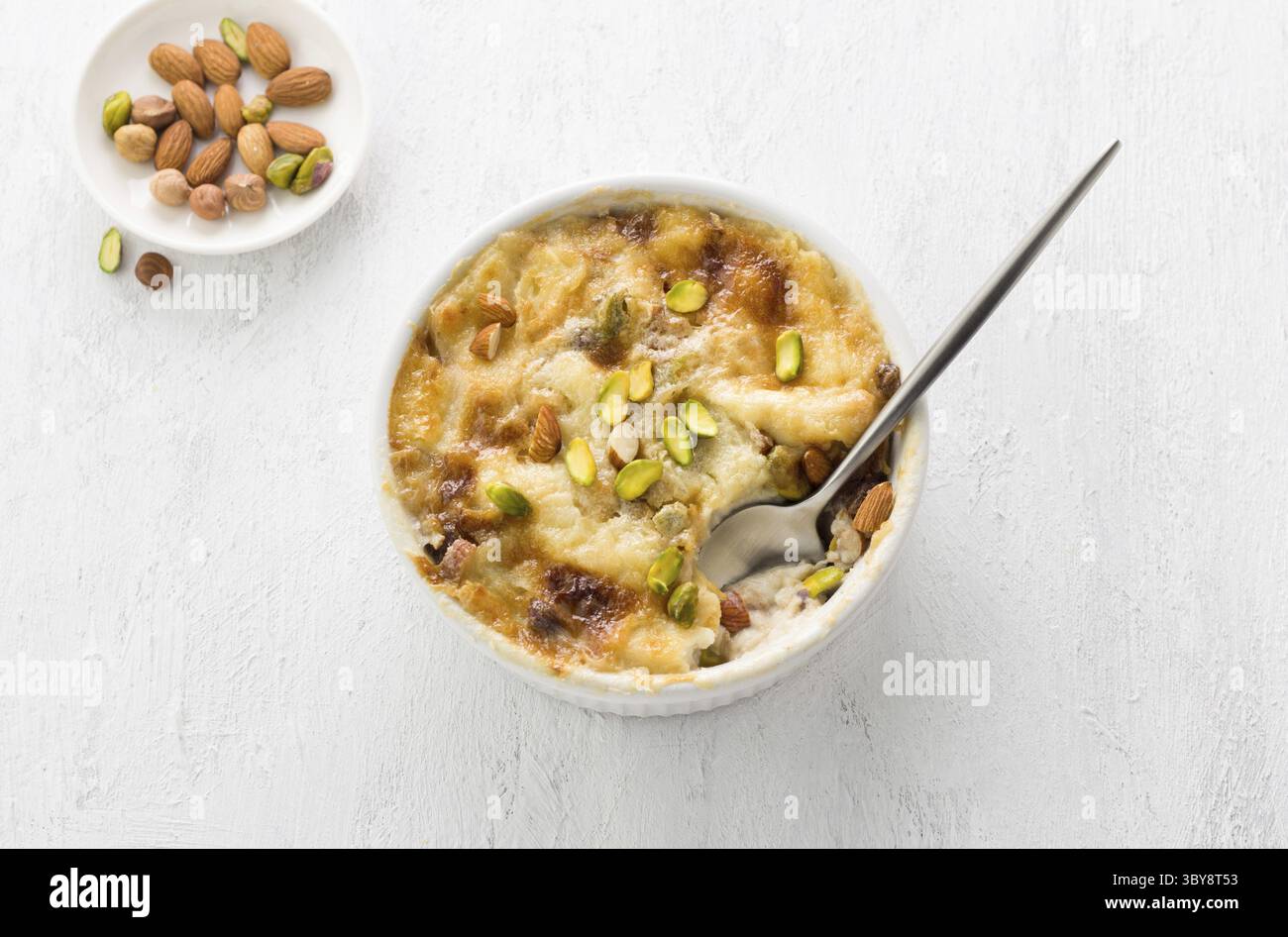 Nourriture, dessert arabe traditionnel Umm Ali dans une forme de céramique blanche décorée de noix sur un fond gris clair, vue de dessus Banque D'Images