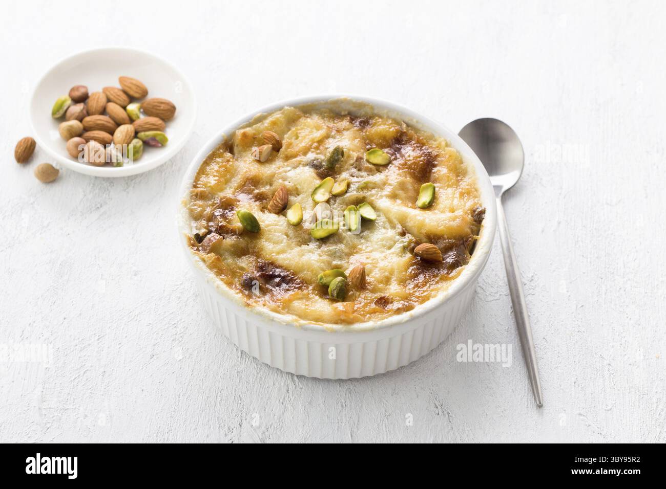Nourriture, dessert arabe traditionnel Umm Ali dans une forme de céramique blanche décorée de noix sur un fond gris clair Banque D'Images