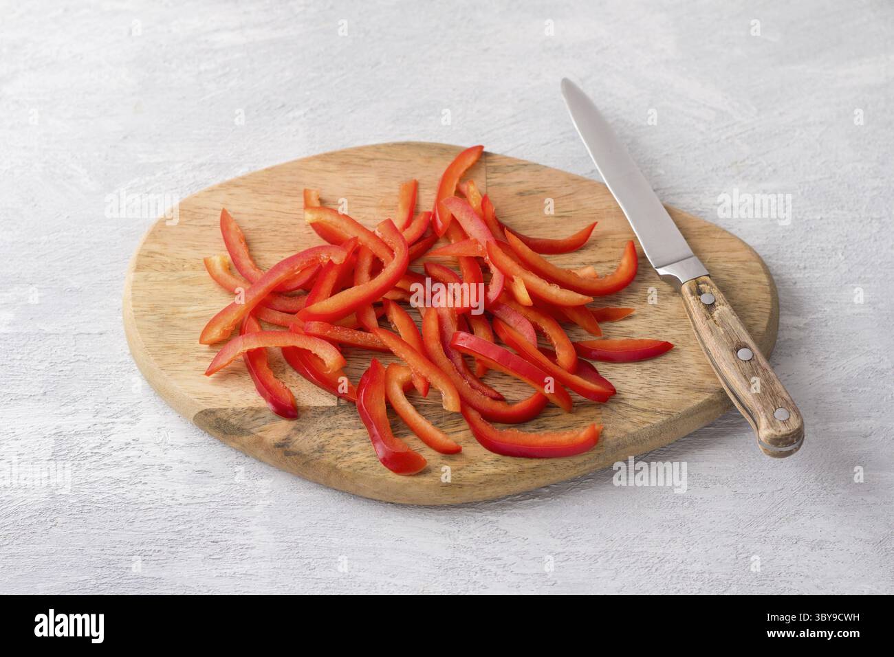 Nourriture, planche de bois avec des poivrons rouges doux hachés sur un fond gris clair, vue de dessus. Étape de cuisson d'aliments végétaliens sains Banque D'Images