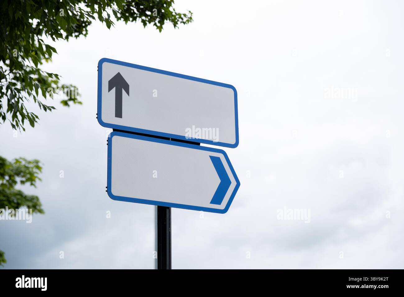 Un double panneau de direction bleu contre un ciel blanc clair contenant des flèches vers le haut et latérales avec des lettres supprimées pour être modifiable pour l'image conceptuelle. Banque D'Images