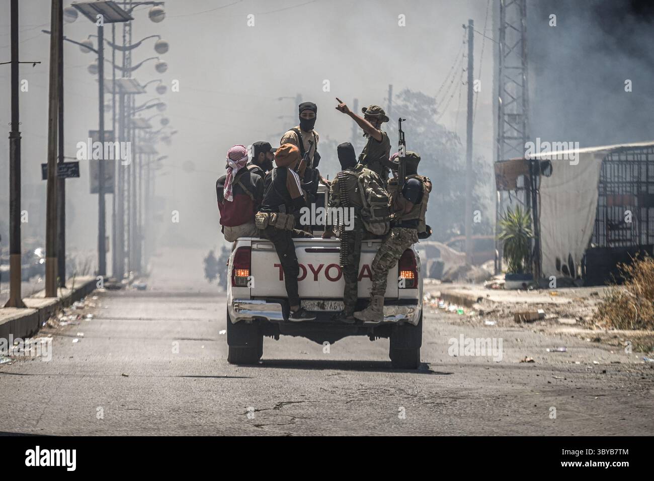 Comme Suwayda, Syrie. 19 juillet 2025. Des combattants bédouins et tribaux se rassemblent dans un véhicule dans la ville d'as-Suwayda, alors que de la fumée s'élève des maisons en feu au milieu d'affrontements entre combattants tribaux et factions druzes locales dans le sud de la Syrie. La peur et le choc envahissent la province à la suite de l'escalade des affrontements isolés qui est devenue l'une des flambées de violence les plus meurtrières que la région ait connues depuis des années. Crédit : Moawia Atrash/dpa/Alamy Live News Banque D'Images
