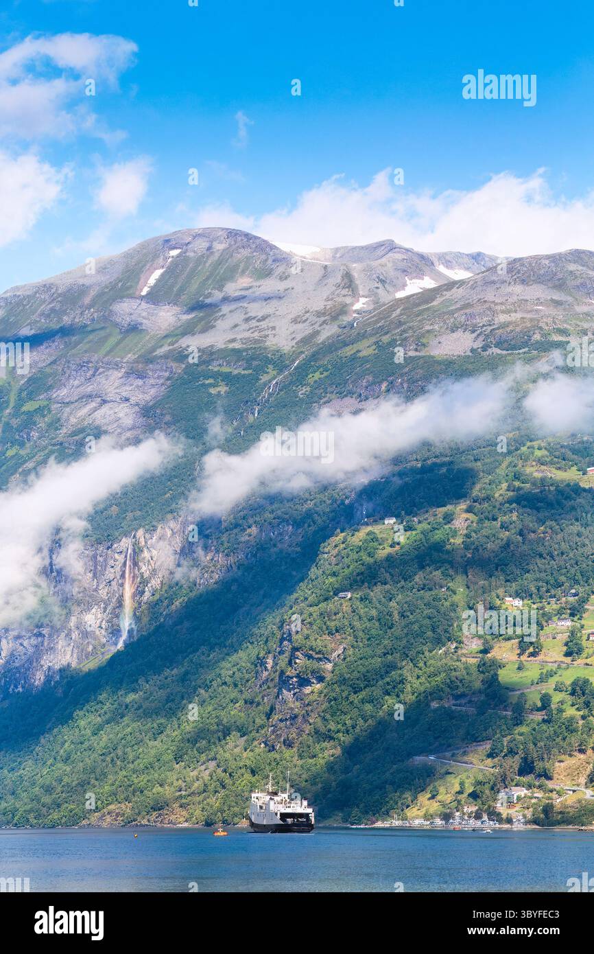 Falaises abruptes, vallée verdoyante et ferry de croisière dans le spectaculaire Geirangerfjord. Sommets norvégiens imposants sous le ciel bleu et les nuages d'été. Norvège. Banque D'Images
