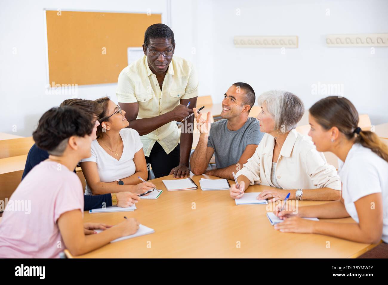 Sympathique tutrice afro-américaine d'anglais donnant des cours de langue à un groupe d'adultes Banque D'Images