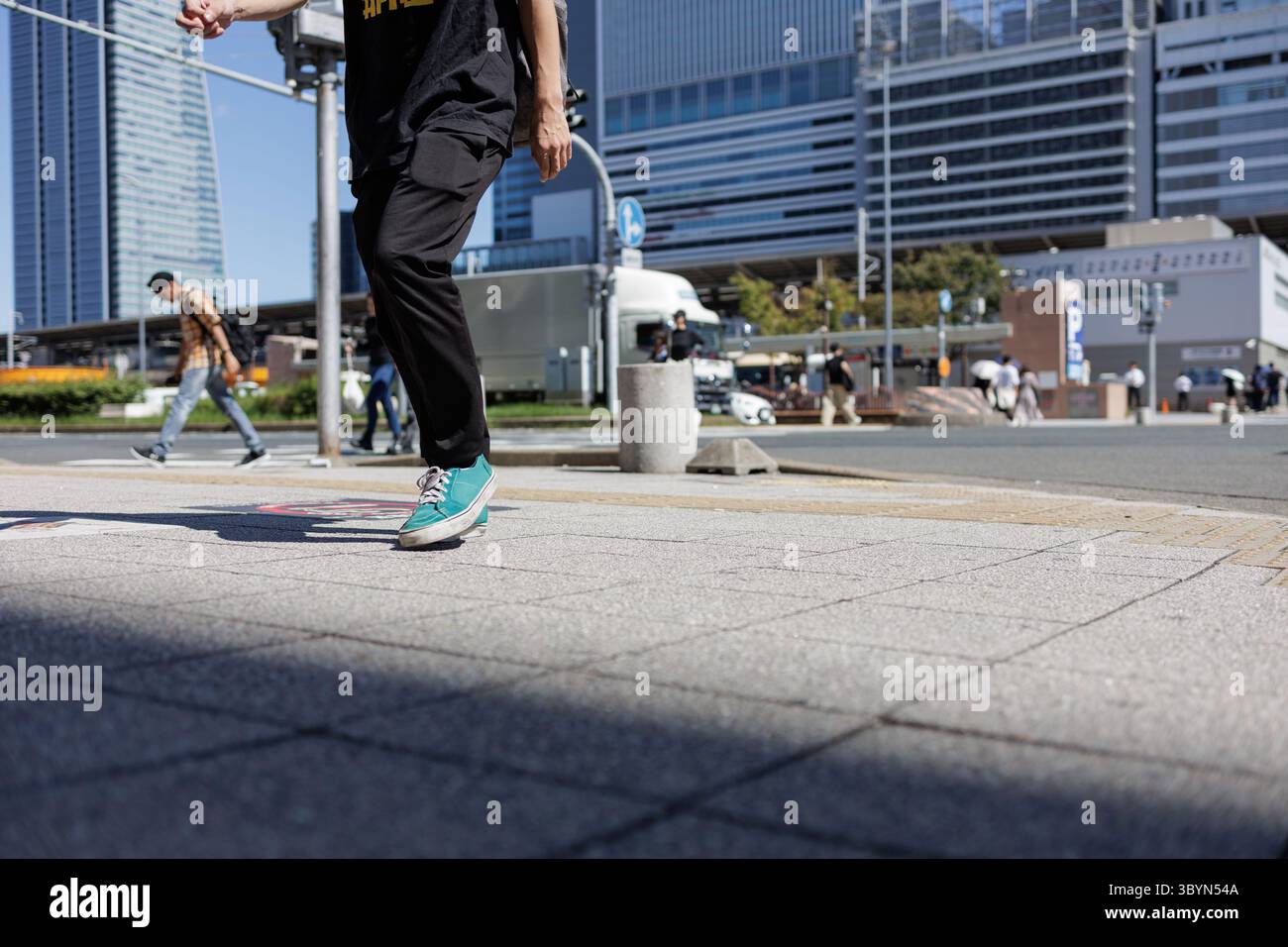 Les gens traversent une grande intersection urbaine avec une architecture moderne en toile de fond. Portant des baskets et des vêtements décontractés, scène représente l'essence du temps de loisirs. Banque D'Images