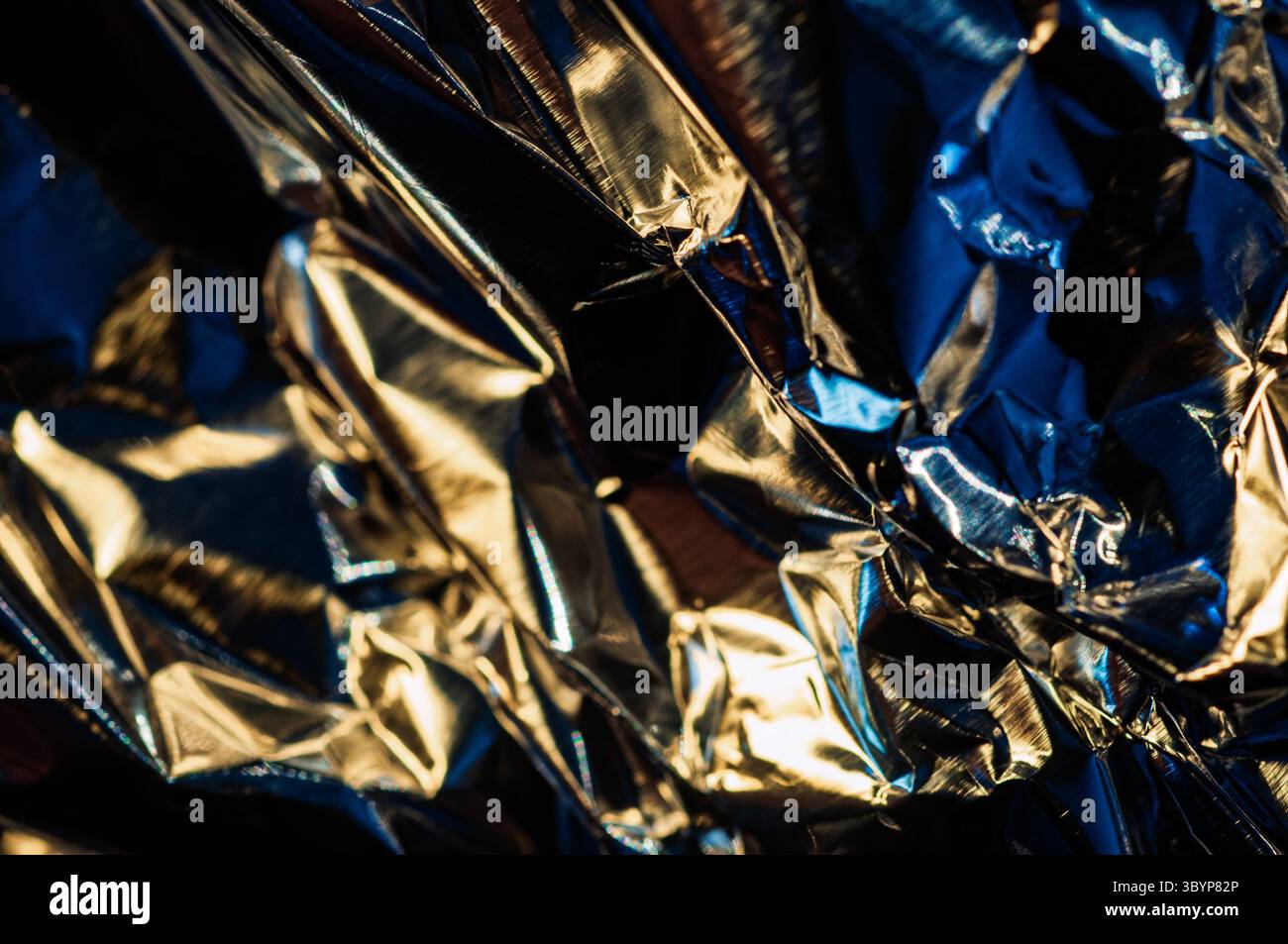 Un gros plan révèle les plis complexes et les surfaces chatoyantes du papier d'aluminium froissé. Le jeu de la lumière et de l'ombre crée une texture dynamique Banque D'Images