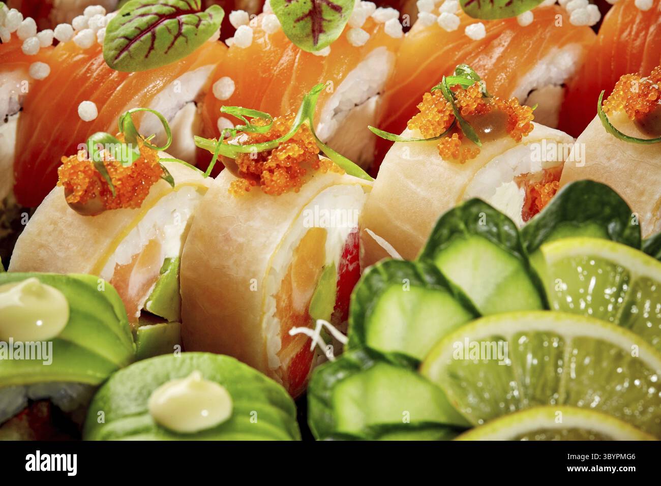 Gros plan dynamique de rouleaux de sushi assortis avec saumon, avocat et mamenori, garnis de tobiko, concombre et tranches de citron vert. Style asiatique populaire Banque D'Images