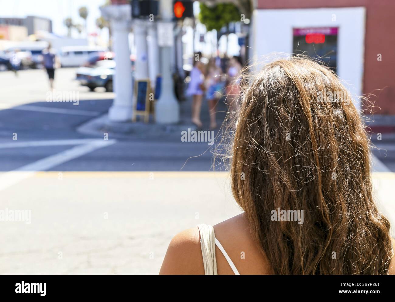 Une jeune femme prête pour la plage attend à un feu rouge. De l'autre côté de la rue, un groupe de jeunes femmes attend, probablement qu'elles bel Banque D'Images