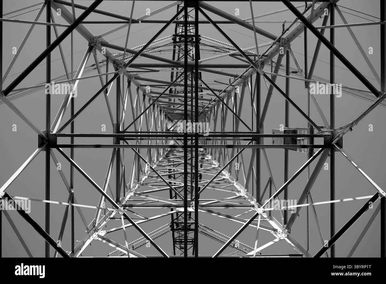 En regardant à travers la toile d'acier d'un pylône de transmission haute tension imposant, on découvre une géométrie de treillis complexe qui s'envole dans un ciel bleu clair aujourd'hui. Banque D'Images