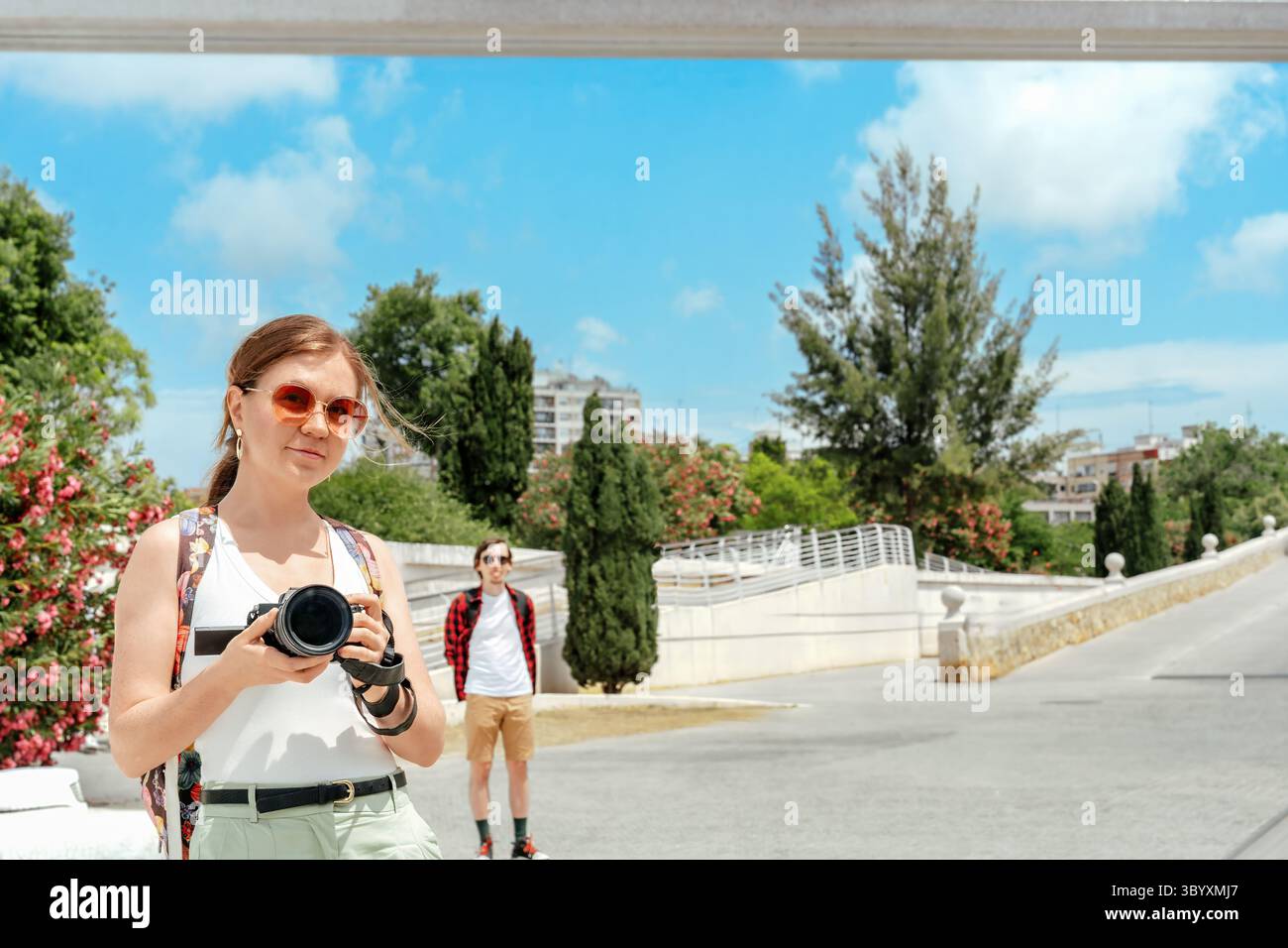 Femme souriante avec appareil photo dans les mains prenant photo selfie avec partenaire en vacances en plein air dans le parc verdoyant ensoleillé à Valence, espace de copie Banque D'Images
