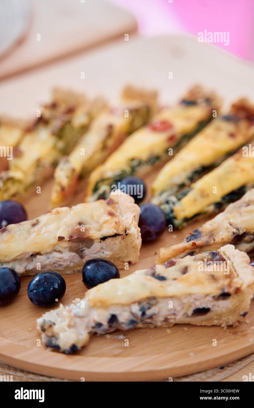 Un délicieux assortiment de tartes salées aux épinards et au fromage garni de myrtilles fraîches, élégamment présentées sur une planche de bois rustique. parfait Banque D'Images