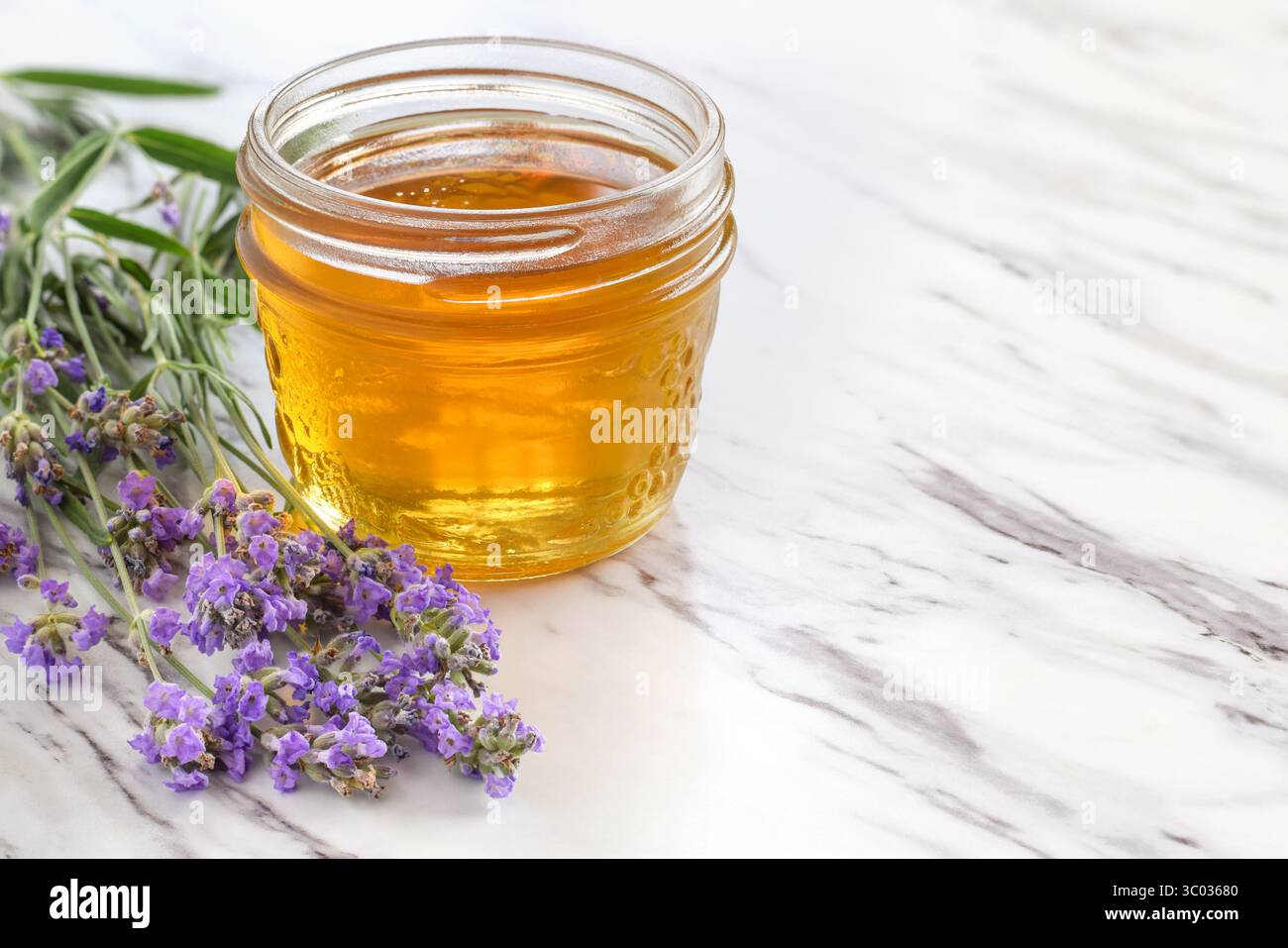 Pot en verre avec des fleurs de miel et de lavande sur la surface de marbre Banque D'Images