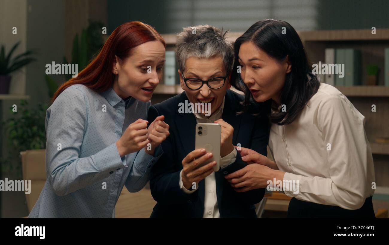 Heureux femmes excitées collègues groupe d'équipe tenant téléphone mobile multinationale lire de bonnes nouvelles femmes d'affaires gagnant la finance en ligne célébrant le bureau Banque D'Images