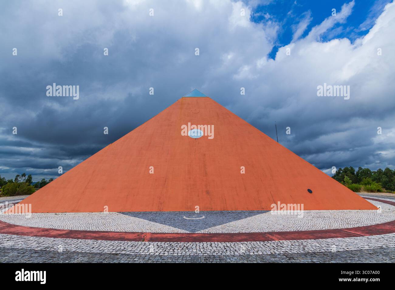 Une pyramide rouge audacieuse se dresse contre un ciel spectaculaire, entourée d'un sentier pavé et d'une végétation luxuriante Banque D'Images