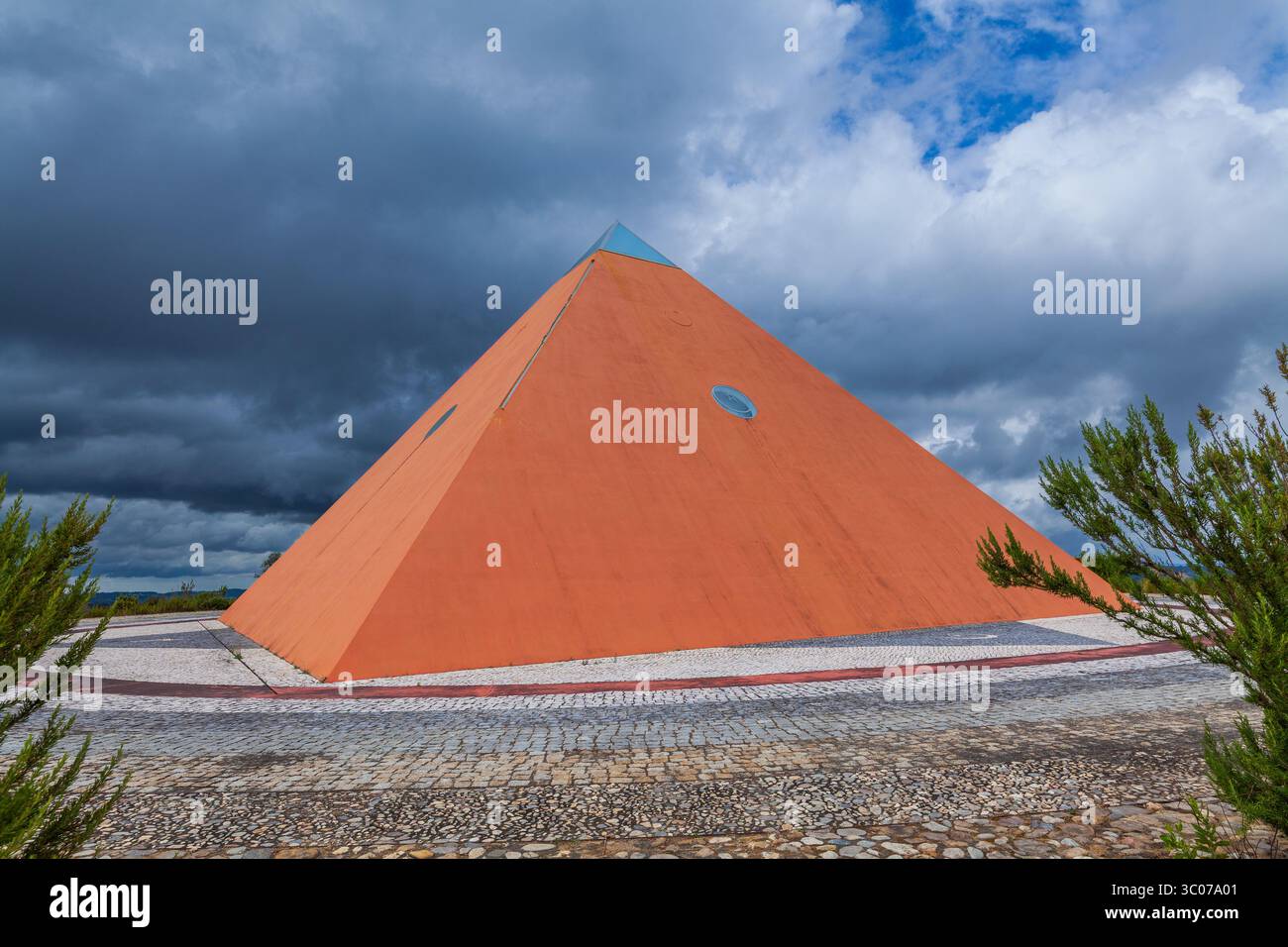 Une pyramide rouge audacieuse se dresse contre un ciel spectaculaire, entourée d'un sentier pavé et d'une végétation luxuriante Banque D'Images