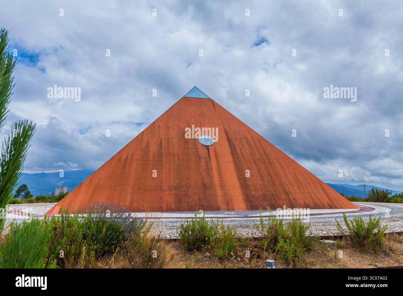 Une pyramide rouge audacieuse se dresse contre un ciel spectaculaire, entourée d'un sentier pavé et d'une végétation luxuriante Banque D'Images