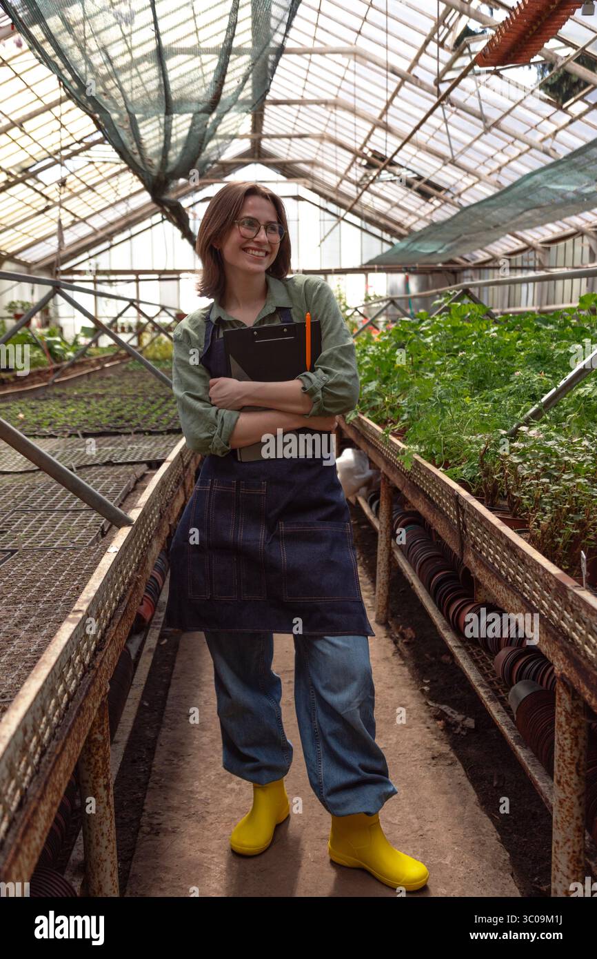 femme dans le tablier et les bottes profite d'un moment joyeux en serre. Banque D'Images