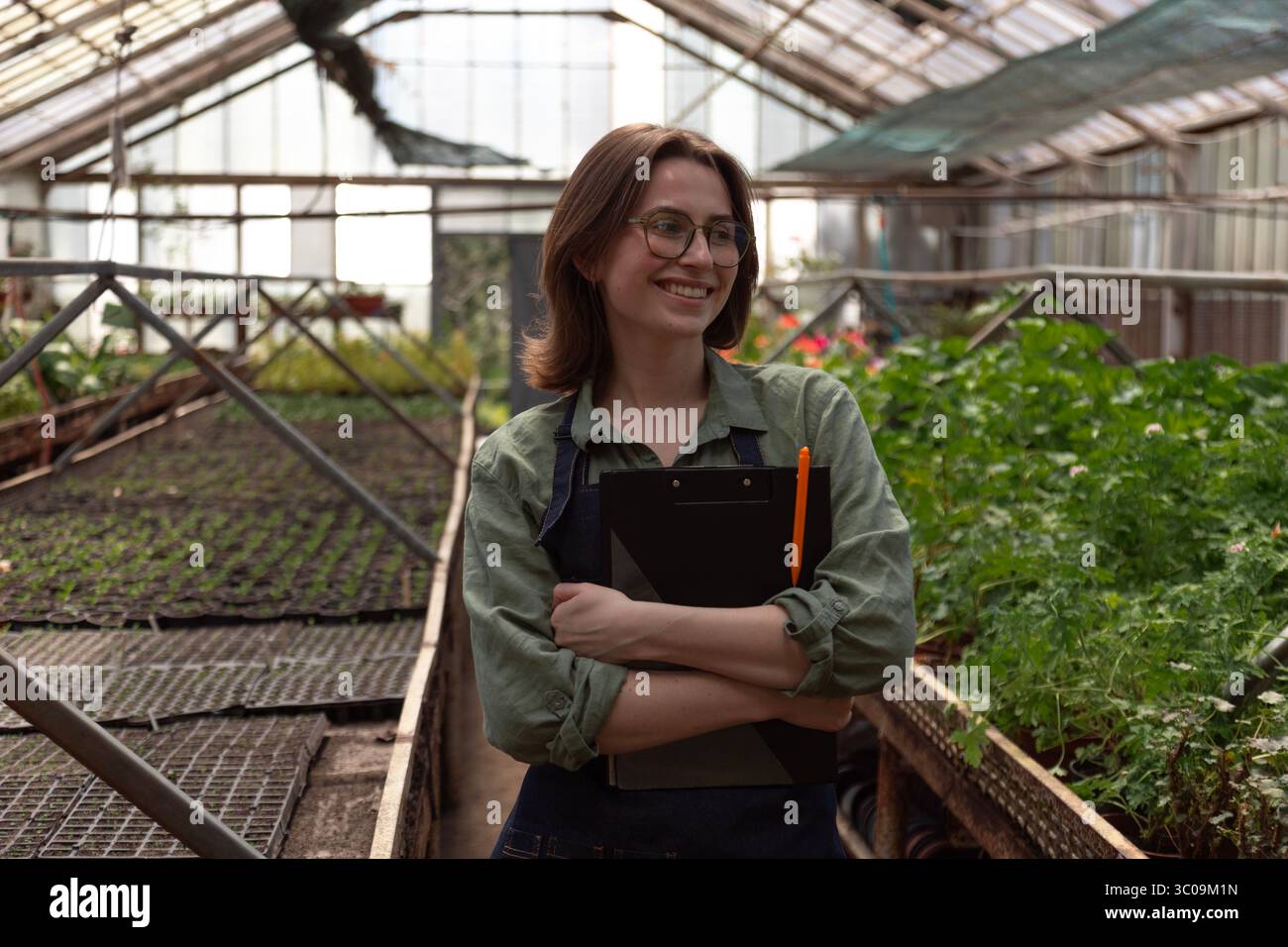 Le travailleur de serre souriant se tient parmi les rangées de plantes luxuriantes Banque D'Images