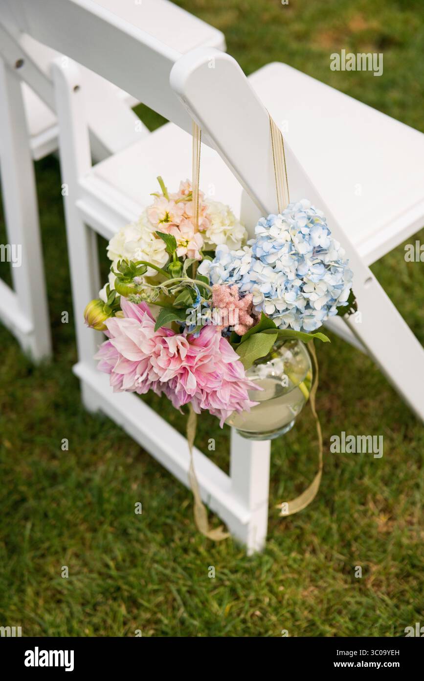Fleurs de cérémonie pastel suspendues sur la chaise de mariage blanche Banque D'Images
