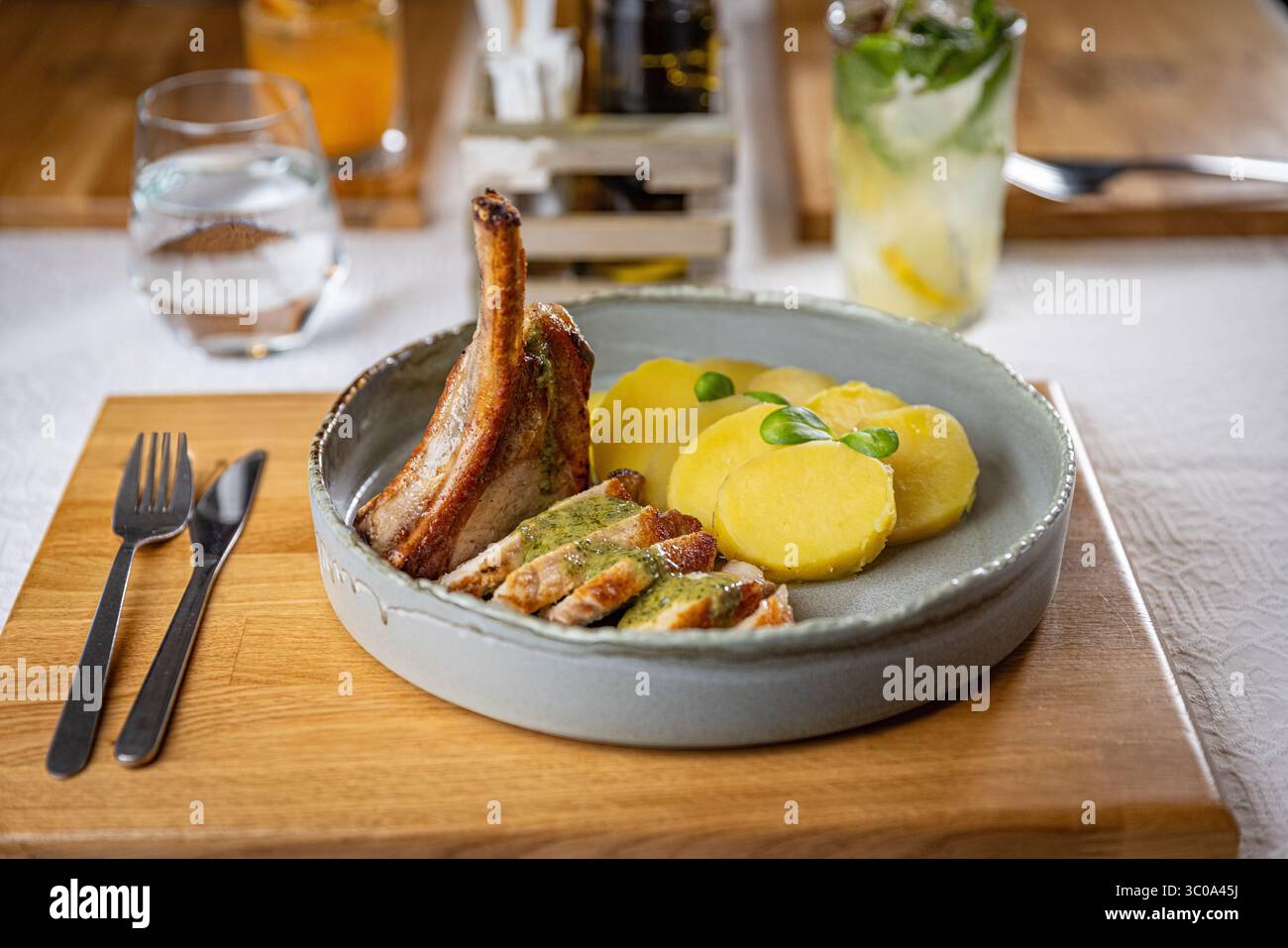 Délicieuse côtelette de porc grillée servie avec tranches de pommes de terre et sauce pesto, accompagnée d'une boisson rafraîchissante Banque D'Images