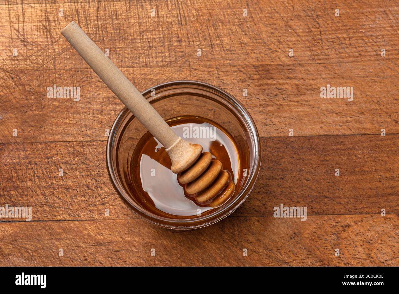 Miel dans un bol en verre avec un plongeur de miel sur fond en bois, vue d'angle. Miel naturel. Banque D'Images