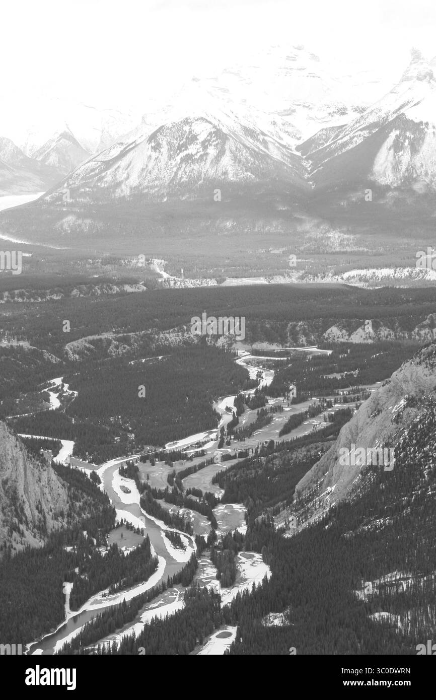 Une vue aérienne montre une rivière serpentant à travers une vallée, entourée de forêts denses et de montagnes enneigées en arrière-plan, mettant en valeur la nature Banque D'Images