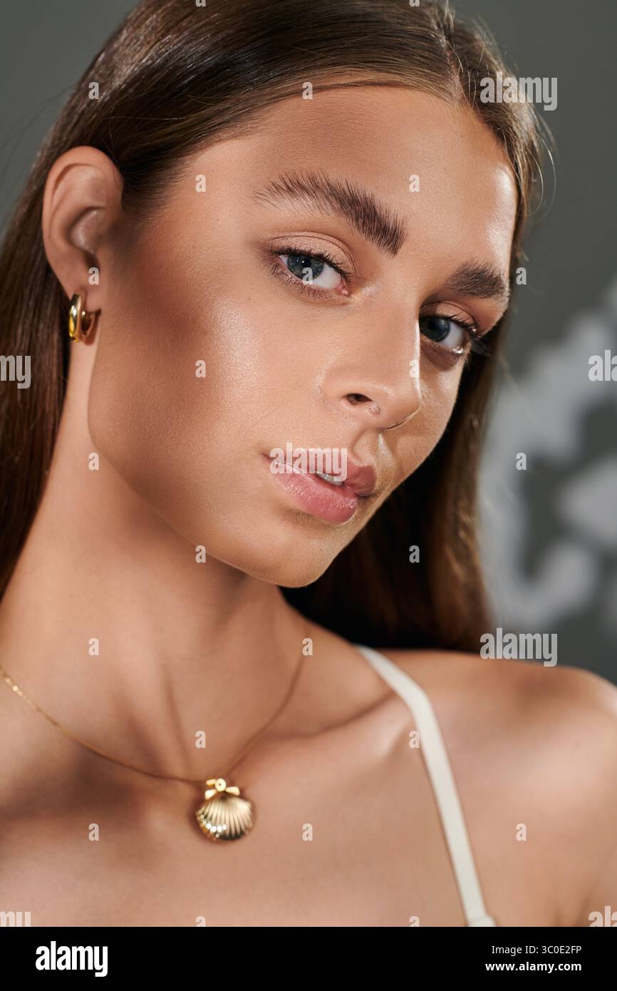 Une jeune femme à la peau bronzée met en valeur sa beauté naturelle tout en posant sur un fond gris. Banque D'Images