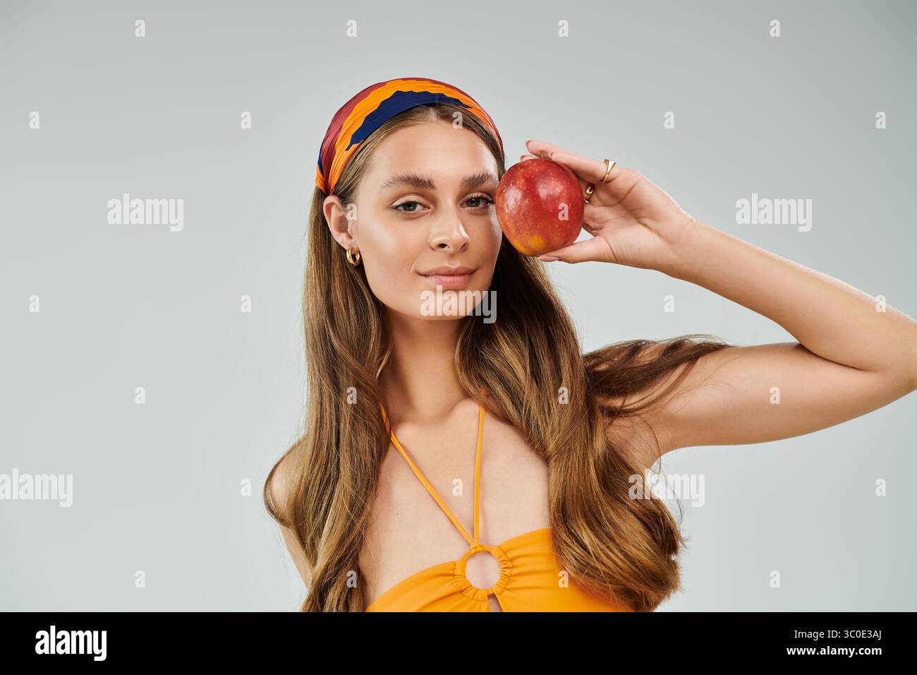 Une jeune femme élégante pose en toute confiance dans une tenue d'été colorée, tenant une pomme rouge. Banque D'Images