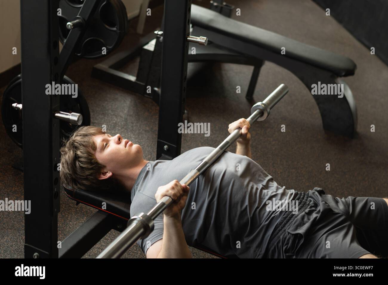 Vue en angle élevé du jeune homme caucasien faisant un exercice de presse de banc avec barre dans la salle de gym moderne. Échauffement. Entraînement thoracique Banque D'Images