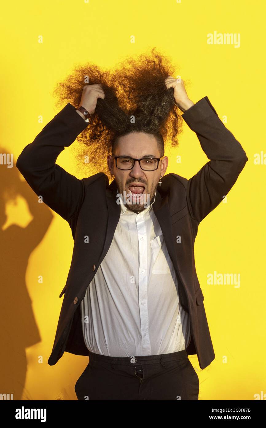 Portrait d'un homme d'affaires stressé aux cheveux longs tirant ses cheveux sur fond jaune Banque D'Images