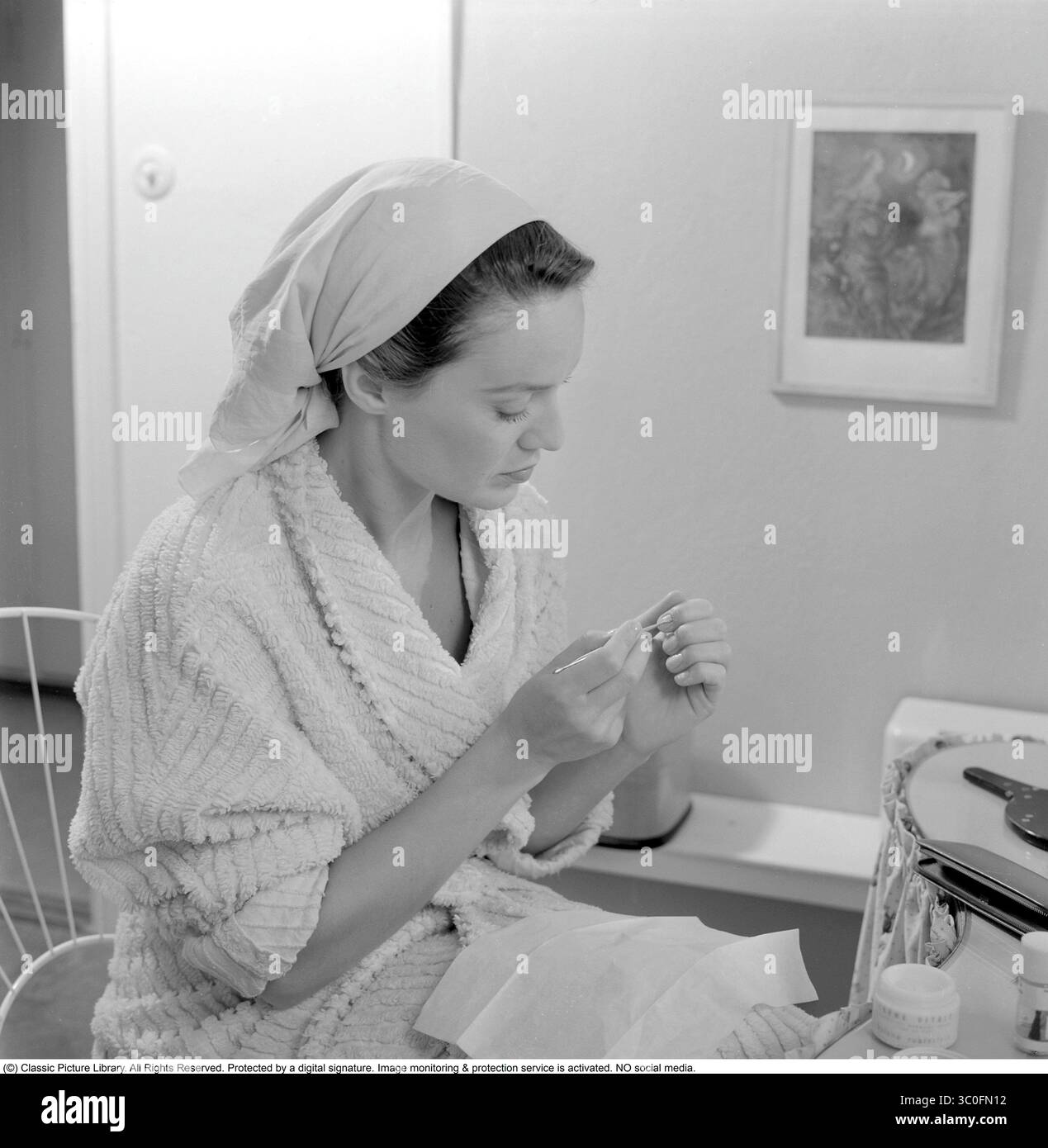 À l'aide d'un poussoir à cuticules 1956. Elle est l'actrice Gaby Stenberg (1923-2011). Un pousseur de cuticules, souvent un petit outil en métal ou en bois, est utilisé pour repousser doucement et nettoyer les cuticules autour des ongles. Il a généralement une extrémité plate et inclinée conçue pour soulever et glisser sous la cuticule - la fine couche de peau à la base de l'ongle - lui permettant d'être soigneusement repoussée pour exposer le lit de l'ongle. Certaines versions disposent également d'une extrémité pointue ou écaillée pour nettoyer la saleté ou la peau morte des bords de l'ongle. Le processus nécessite un toucher doux pour éviter d'endommager la peau délicate, souvent après avoir trempé le finge Banque D'Images