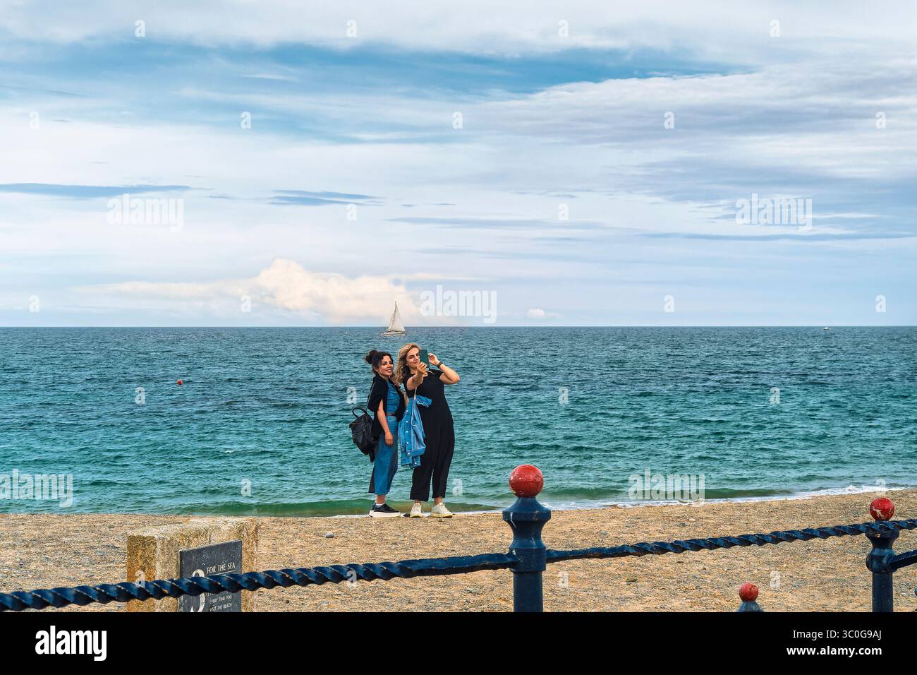Deux femmes posent et font des selfies à Bray Beach pendant le BBQ Festival, avec vue sur la mer et ciel spectaculaire – 19.07.2025 Banque D'Images